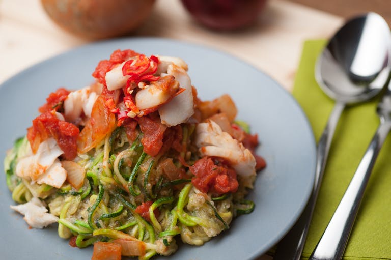A plate of zucchini noodles topped with fresh tomato and fish, ideal for a healthy meal.