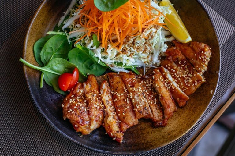 A savory chicken salad bowl garnished with sesame seeds, fresh vegetables, and lemon wedge.